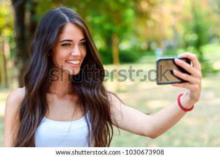 Young beauty with long brown hair taking a selfie on smart phone in park