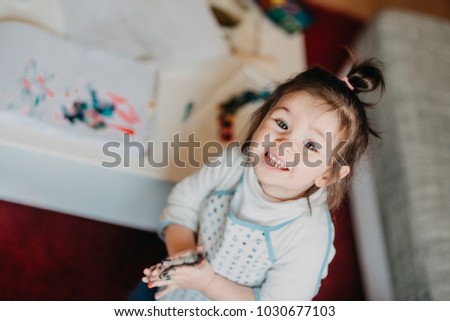 toddler girl in drawing apron draws fingers at home, shows her colored hands