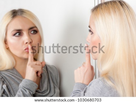 Woman shows silence sign looking at her reflection in the mirror