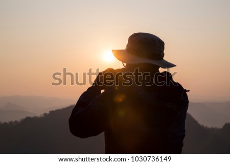 Silhouette Handsome man looking forward with binoculars at a mountain