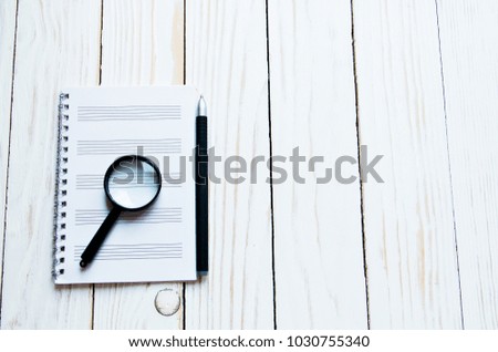 Magnifier notebook, pen on a white wooden backdrop