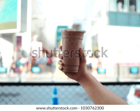 Holds a plastic glass of iced chocolate, blur background with selective focus.