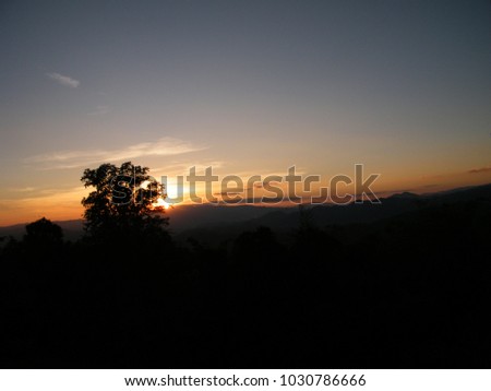 The black silhouette tree appears when the sun rises. The early morning view which has orange sky is beautiful. The sunset sky shows the sun rays through the clouds. The high view of mountain is nice.