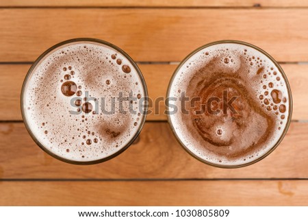 Two mug of beer with bubble foam on glass on top view wooden background 