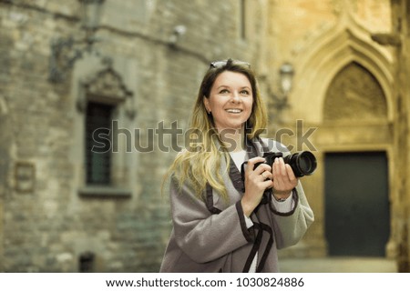 Young cheerful woman with camera looking curious and taking pictures outdoors