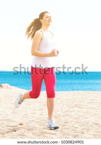 Young sporty woman running on beach by ocean in morning