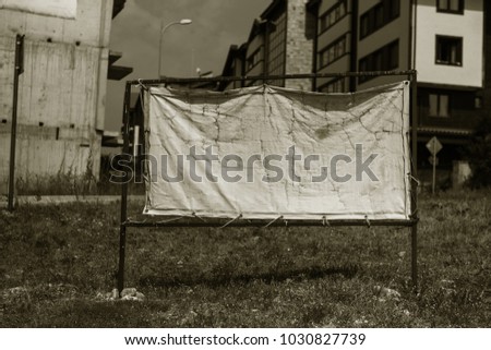 Old shabby, sun-blown SALE banner against the backdrop of abandoned construction of a house, hotel. House for sale. Real estate sign in front of the house. Sold House, Sale