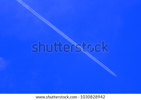 Defocus faraway long jet trail of white vapor or steam generated by jet engine plane fast speeding from upper left to bottom right on dark blue sky and fade cloud. Aircraft head directly to south east
