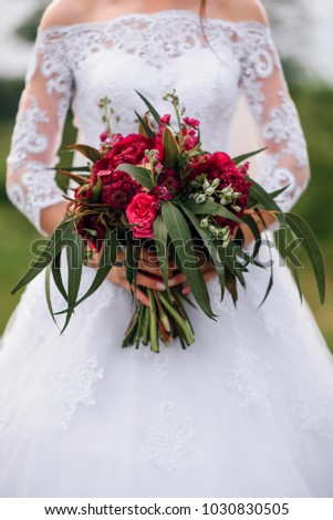 wedding bouquet with red peonies in the hands of the bride in a white elegant dress