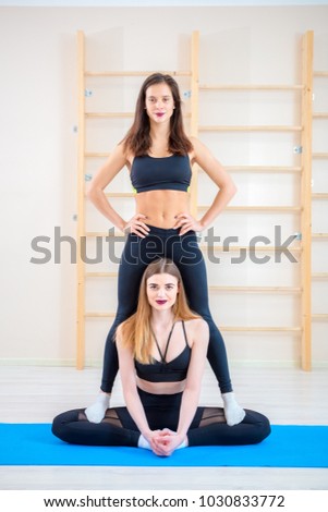 brunette is standing on leg of  blonde in  exercise butterfly in gym