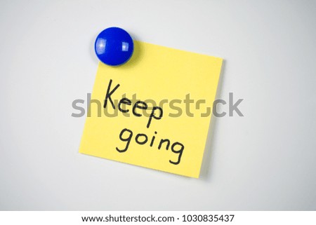 Yellow sticker inscription 'Keep going' attached to a white fridge with a blue magnet  