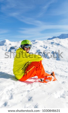 Image of sportive man wearing helmet wearing yellow jacket sitting on snowy slope during day
