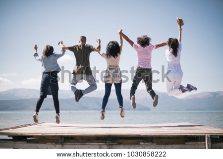 Portrait of young friends jumping from jetty into lake. Friends in mid air on a sunny day at the lake.