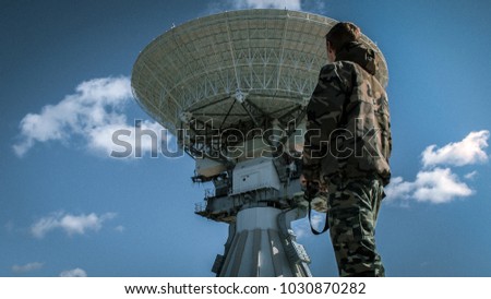 men in camouflage standing in front of huge radio telescope near abandoned soviet military town Irbene, Latvia  Royalty-Free Stock Photo #1030870282