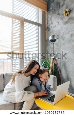 Mother and daughter sitting on the couch and using laptop