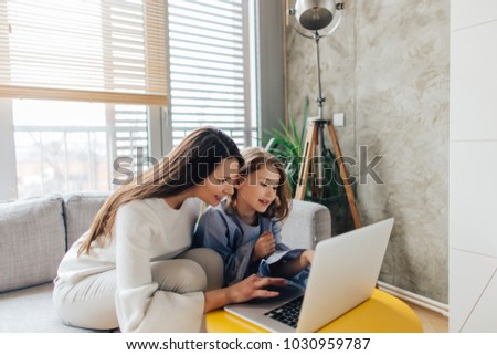 Mother and daughter siting on the couch and using laptop