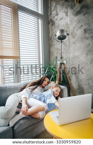 Mother and daughter laying on the couch and using laptop