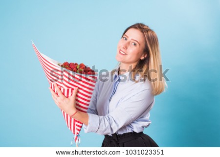 Bouquet of strawberries in the hands of a girl on blue background