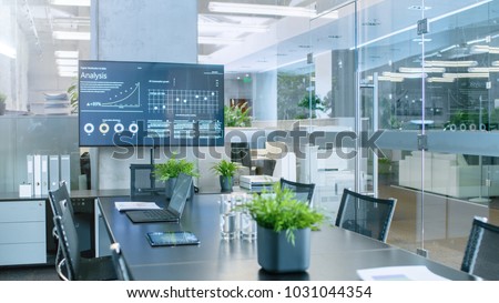 Modern Empty Meeting Room with Big Conference Table with Various Documents and Laptops on it, on the Wall Big TV Showing Company's Growth, Statistics and Pie Charts. Royalty-Free Stock Photo #1031044354