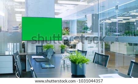 Modern Empty Meeting Room with Big Conference Table with Various Documents and Laptops on it, on the Wall Big TV with Green Chroma Key Screen.