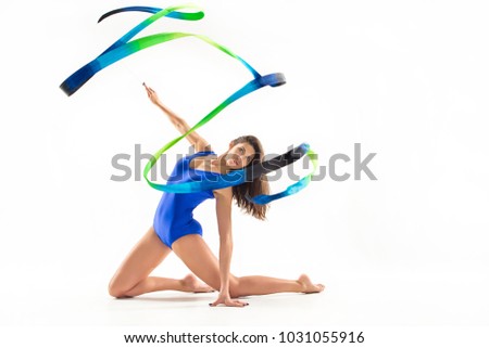The portrait of beautiful young brunette woman gymnast training calilisthenics exercise with blue ribbon on white studio background. Art gymnastics concept. Caucasian model in full height