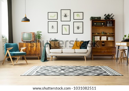 Vintage tv standing on a wooden cabinet next to a comfy couch in a stylish day room interior Royalty-Free Stock Photo #1031082511