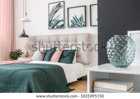 Modern, glass vase in a bedroom interior and a double bed in the background with wool blanket and colorful pillows Royalty-Free Stock Photo #1031095150