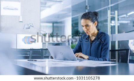 Beautiful Female Data Analyst sitting at the Table Works on a Laptop. Stylish Woman in the Modern Office Environment. Royalty-Free Stock Photo #1031105278