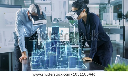 Male and Female Architects Wearing  Augmented Reality Headsets Work with 3D City Model. High Tech Office Professional People Use Virtual Reality Modeling Software Application. Royalty-Free Stock Photo #1031105446