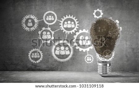 Lightbulb with multiple gears inside placed against social gear structure on grey wall. 3D rendering.