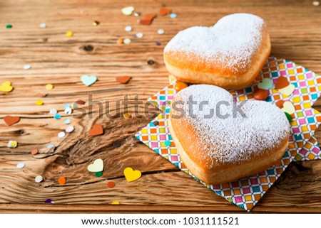 Two romantic heart shaped cakes to celebrate a wedding, Valentines, anniversary or engagement party with scattered confetti on a wooden background with woodgrain texture