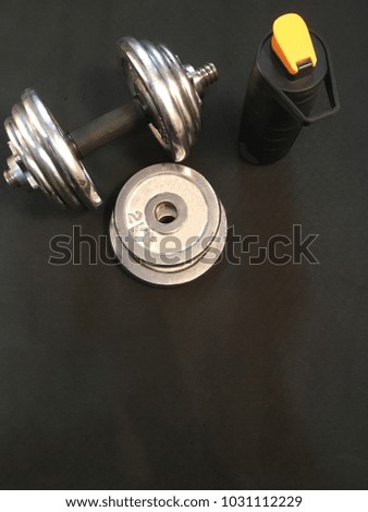 Dumbbell, weights, standing battle of water, on black fitness mat. Top view.