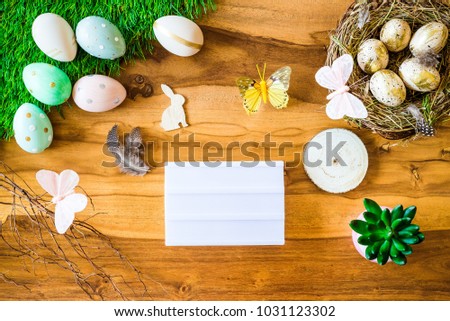 Happy Easter shot from above as flatlay with blank light box for greetings and colorful retro easter eggs, grass, butterfly and easter nest on wooden table