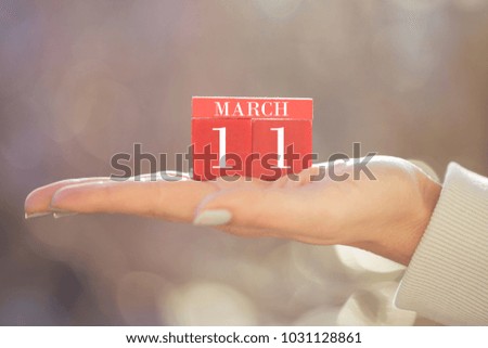 the woman is holding a red wooden calendar. Red wooden cube shape calendar for MARCH 11 with hand