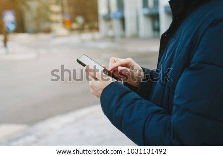 Mans hands typing text message on smart phone. Cropped image of young man stay on the street and using mobile phone.