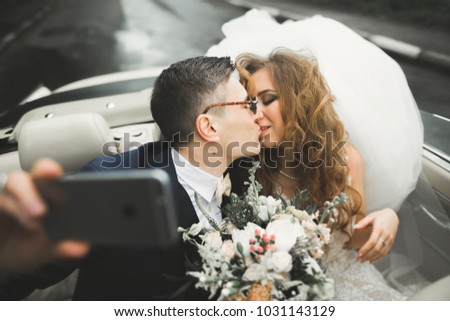 Happy bride and groom making selfie at their wedding in retro car