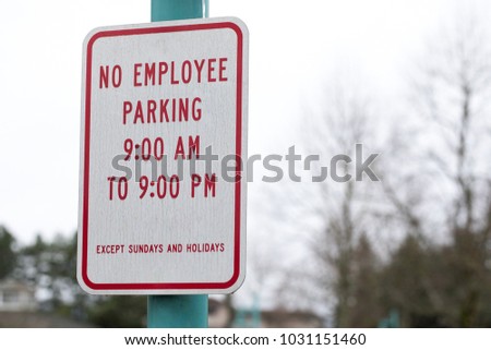 Close up on a red and white sign for No Employee Parking between 9am and 9am, except Sundays and Holidays, in the car park at a mall and shopping center