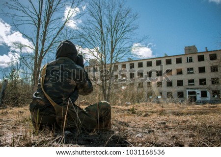 men in camouflage sits on the field front of abandoned building in abandoned soviet military town Irbene, Latvia Royalty-Free Stock Photo #1031168536