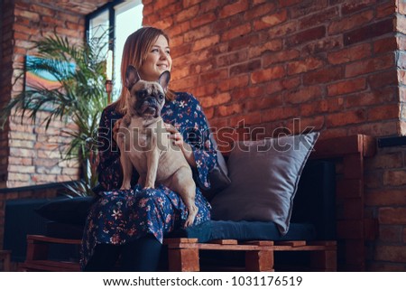 Portrait of a smiling woman sitting with a cute pug in a room wi