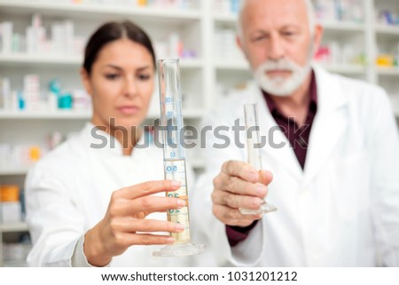 Medicine, pharmaceutics, health care and people concept - Male and female pharmacists holding graduated cylinders with chemicals. Selective focus on foreground