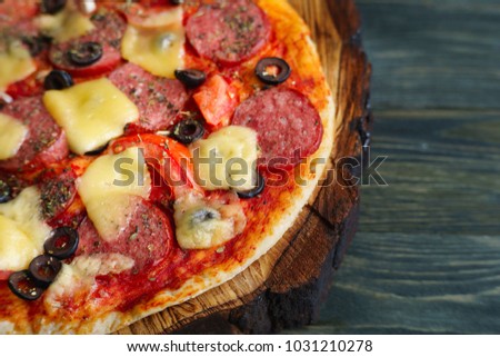 Delicious homemade pizza with salami, olives and tomatoes on chopped wood tray, close up. Italian food