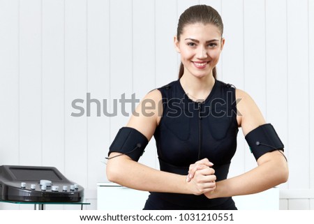Beautiful young girl doing exercises on the machine for muscle stimulation. Innovative technology of exercise and fitness. Exercises for women on the electro-muscular machine.