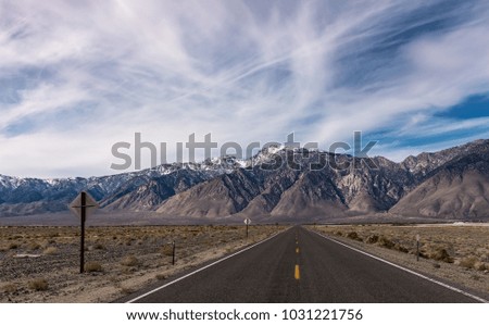 Endless straight empty desert highway with mountain range in the background and dramatic cloudy blue sky.Road trip trough Death Valley in California 