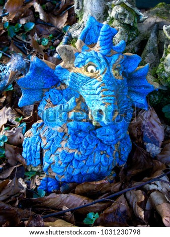 Clay figure of a bright blue dragon in a woodland fantasy garden amid naturally fallen leaves and twigs