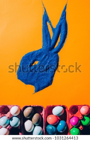 top view of bunny made of blue sand and easter eggs isolated on orange