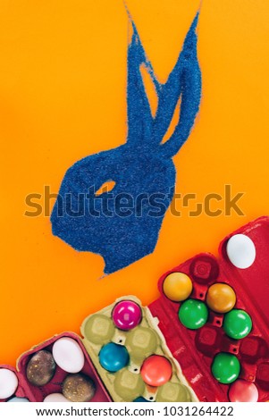 top view of bunny made of blue sand and painted easter eggs isolated on orange