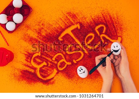 cropped image of woman painting smileys on easter eggs on orange