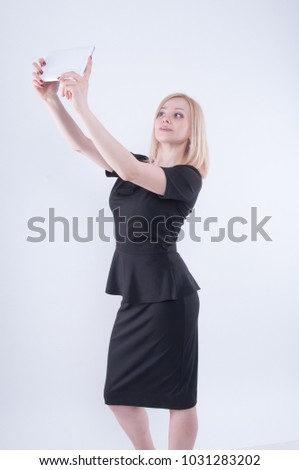 Woman making selfie with tablet on white isolated background. Close up of young blonde beautiful girl in black dress looking in white tablet in her hands
