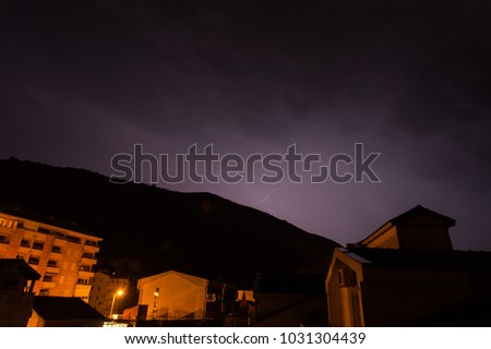 Lightning strikes over night tiled roofs of houses in the mountains of Montenegro