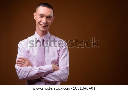 Studio shot of young handsome androgynous businessman wearing pink shirt against brown background